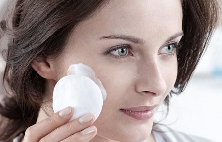 Žena nanosi kremu na lice pamučnim tupferom